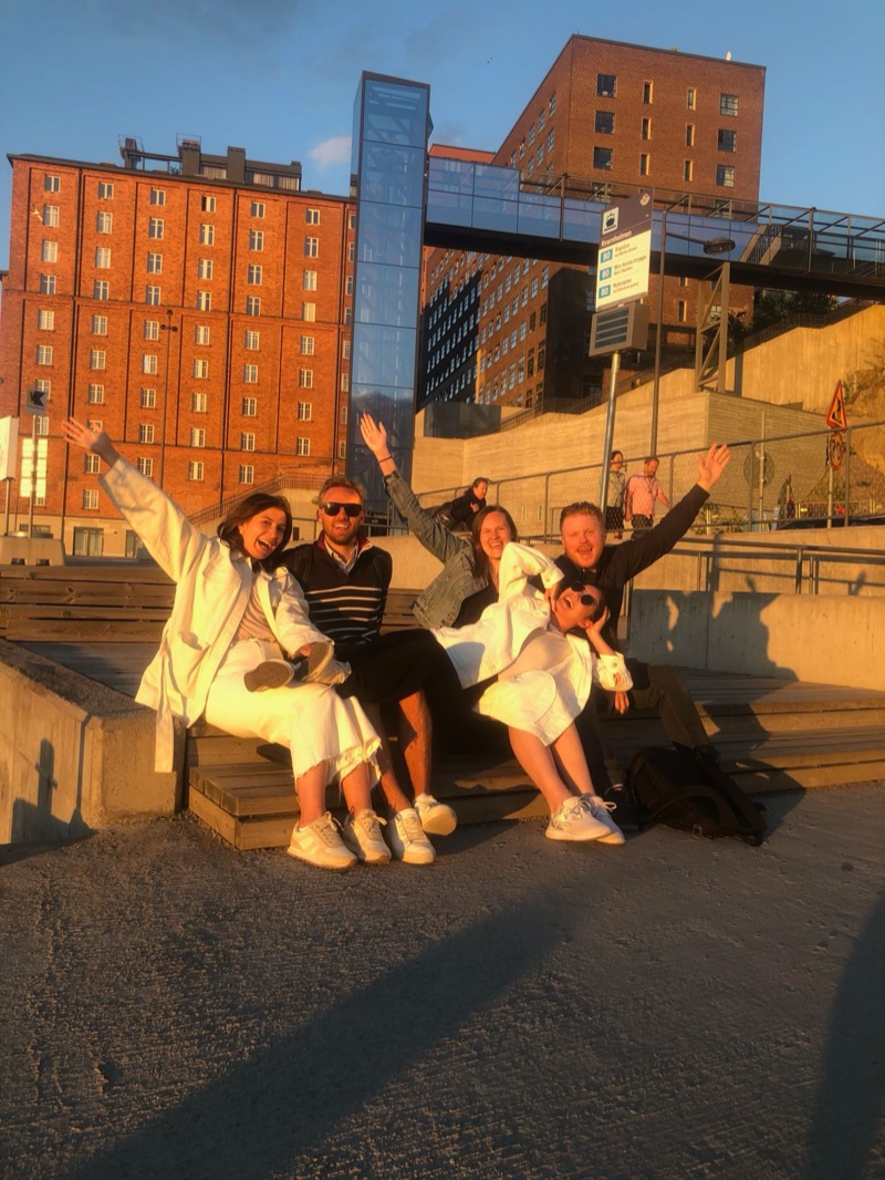 Five people from the early Aimfor team on a bench in evening sun, arms in the air, laughing