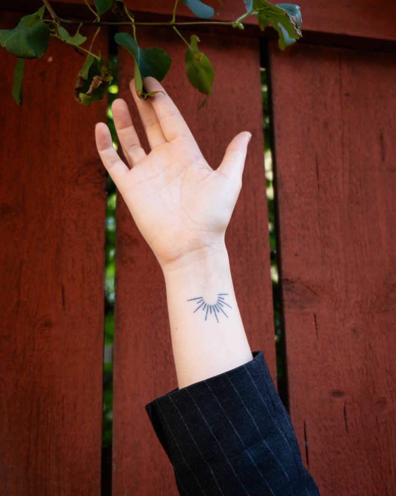 Annelie's open hand raised against a red wooden wall, with a small tattoo on the wrist