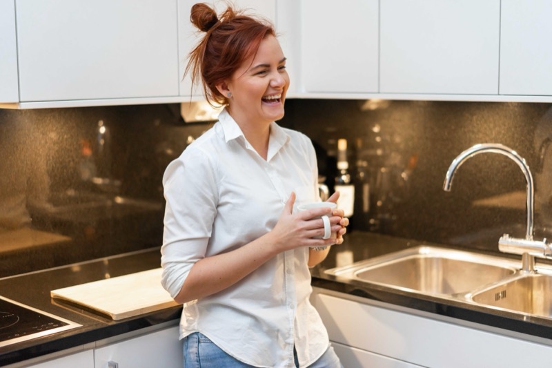 Annelie laughing in her kitchen at home in Stockholm, holding a mug