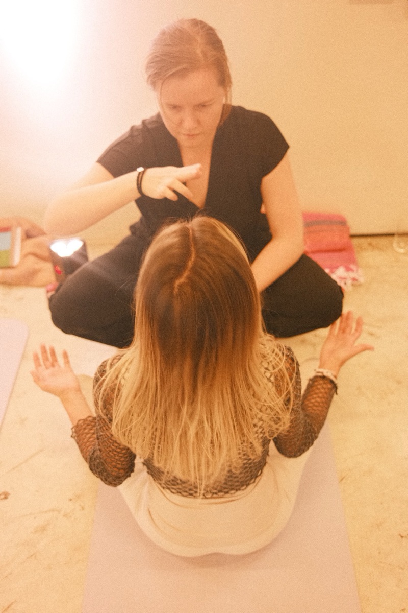 Annelie sitting cross-legged in front of a participant seen from behind, her hand raised above the participant's head