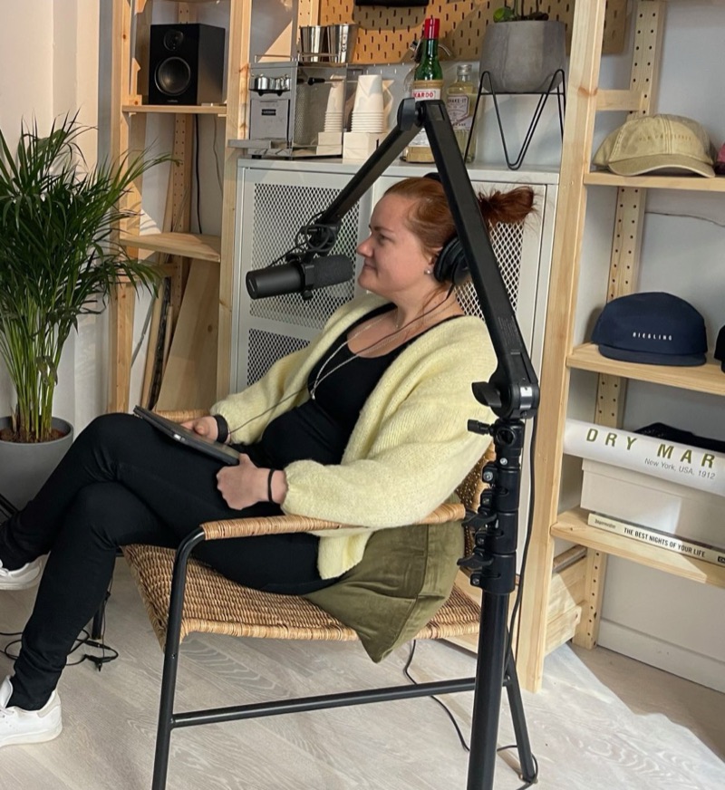 Annelie in a wicker chair with headphones and a studio microphone, recording a podcast