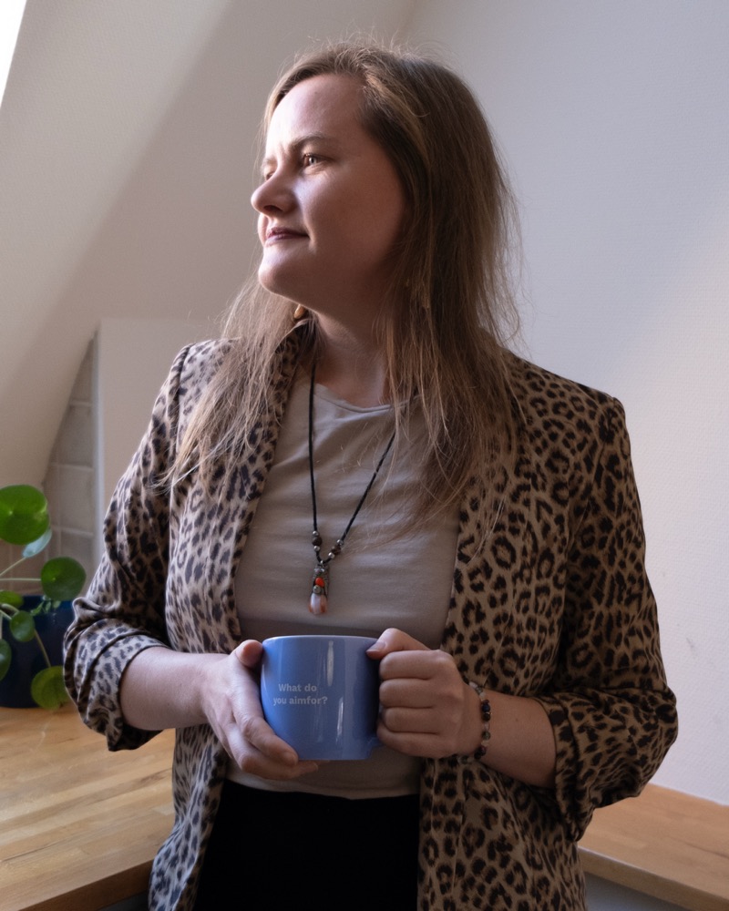 Annelie Näs håller en mugg och ser eftertänksamt ut genom ett fönster