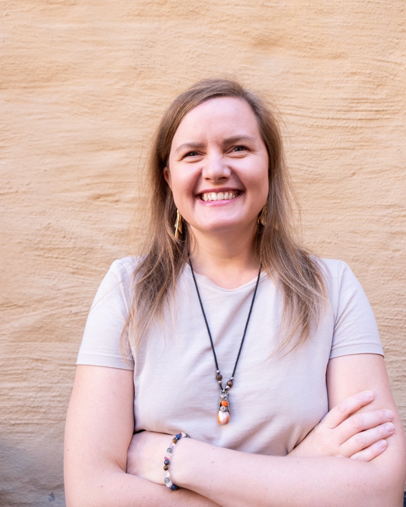 Annelie Näs smiling with her arms crossed in front of a sandstone wall
