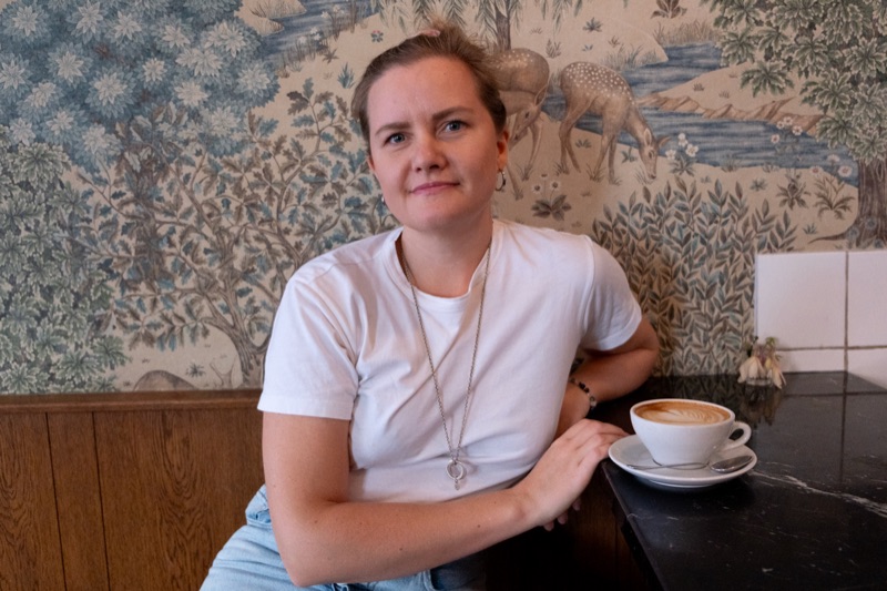 Annelie Näs sitter lugnt vid ett kafébord med en kopp kaffe och ser in i kameran