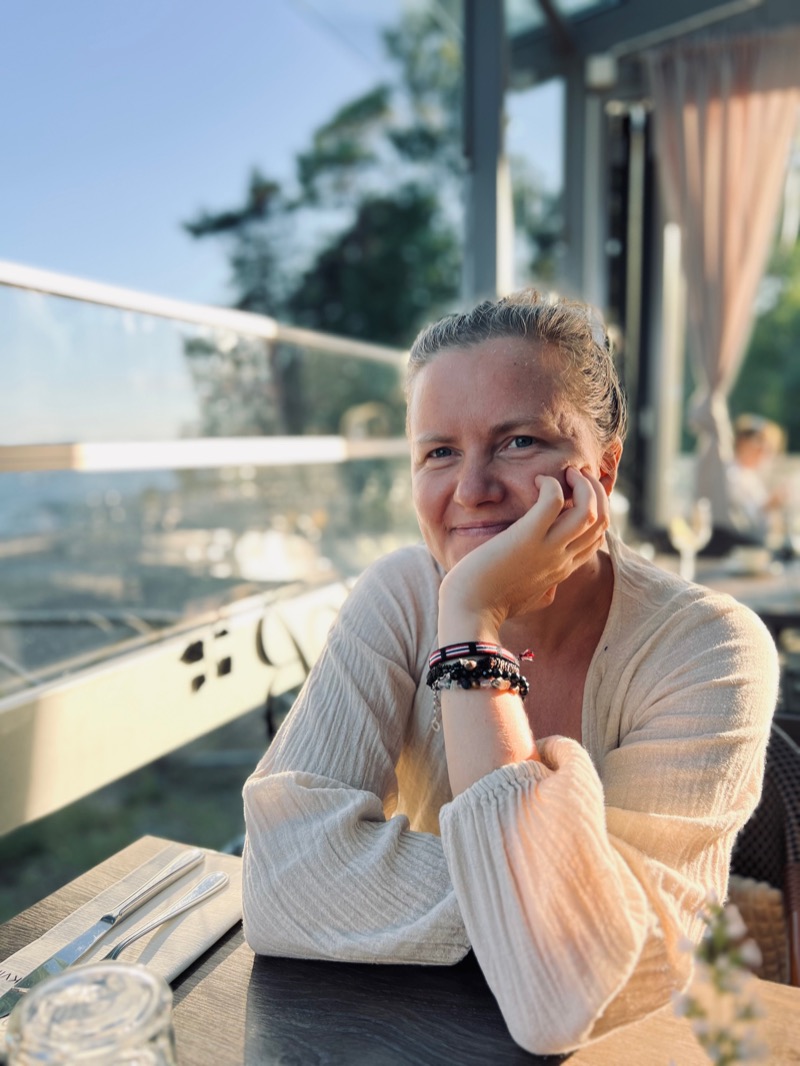 Annelie Näs resting her chin on her hand at a restaurant table by the sea, in warm evening light