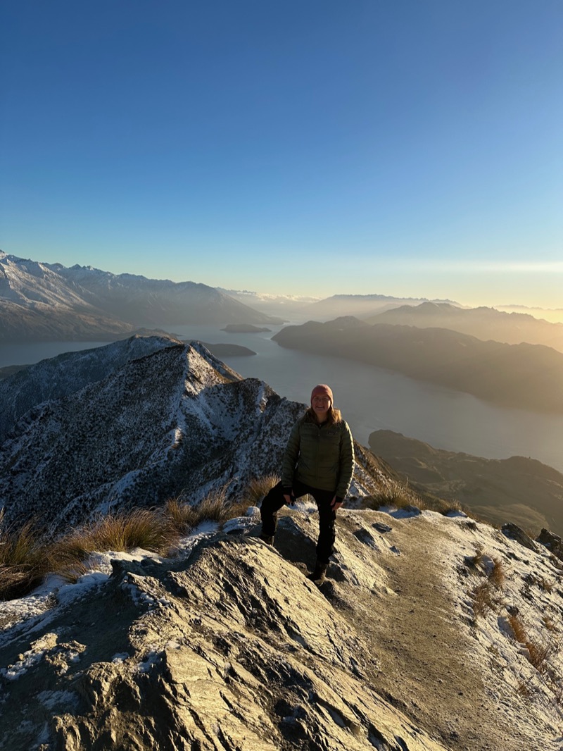 Annelie standing on a frosty mountain ridge at sunrise, high above a lake