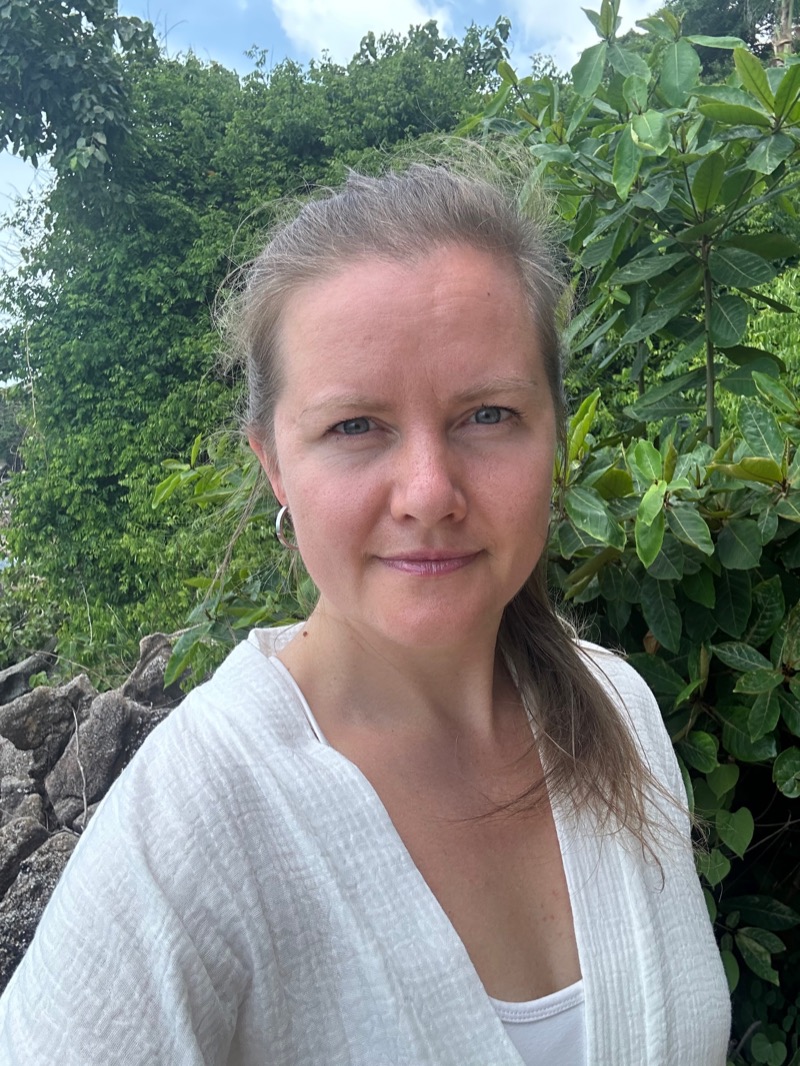Close portrait of Annelie Näs in a white linen shirt, standing among green leaves