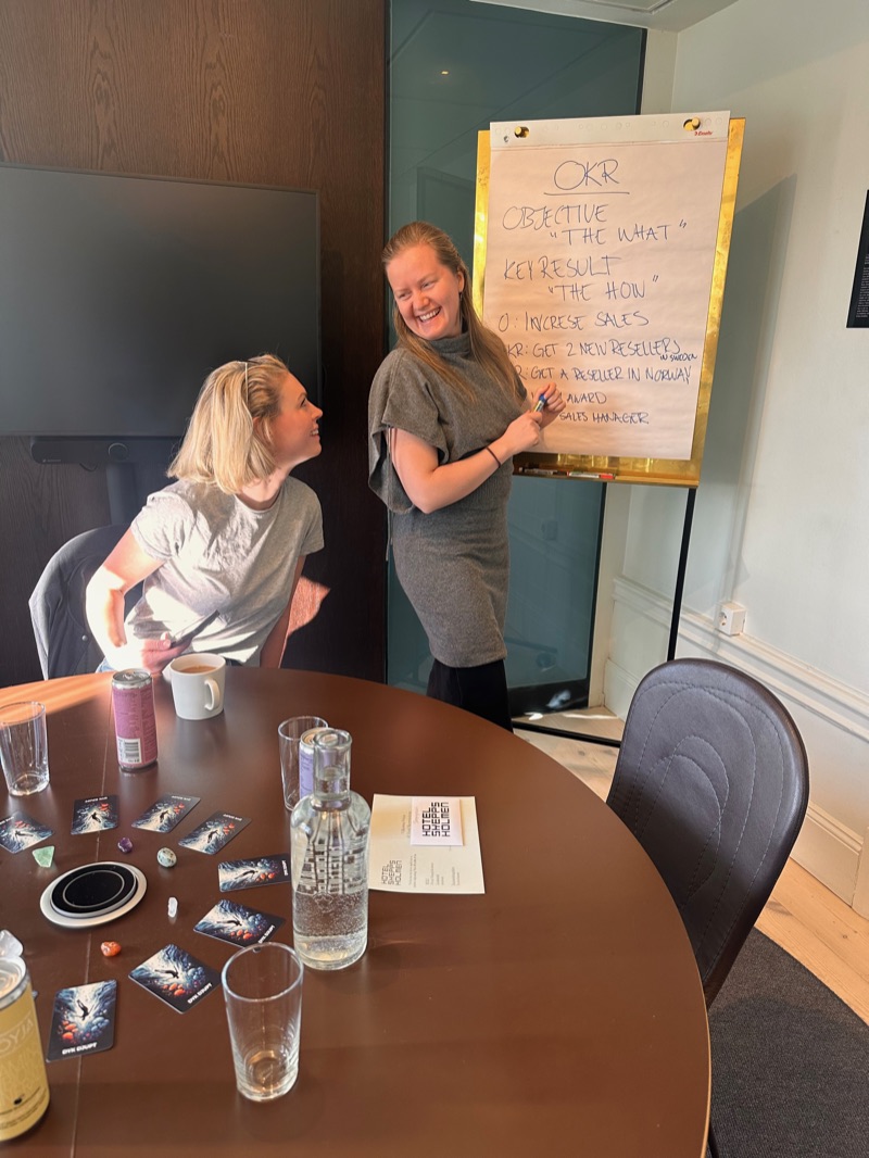 Annelie laughing beside a flipchart during a workshop, turned towards a participant who is looking up at her